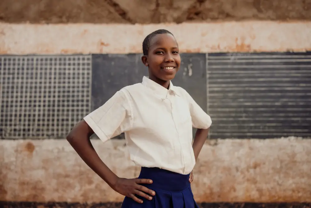 Glory stands tall, hands on her hips and smiling in her school uniform.
