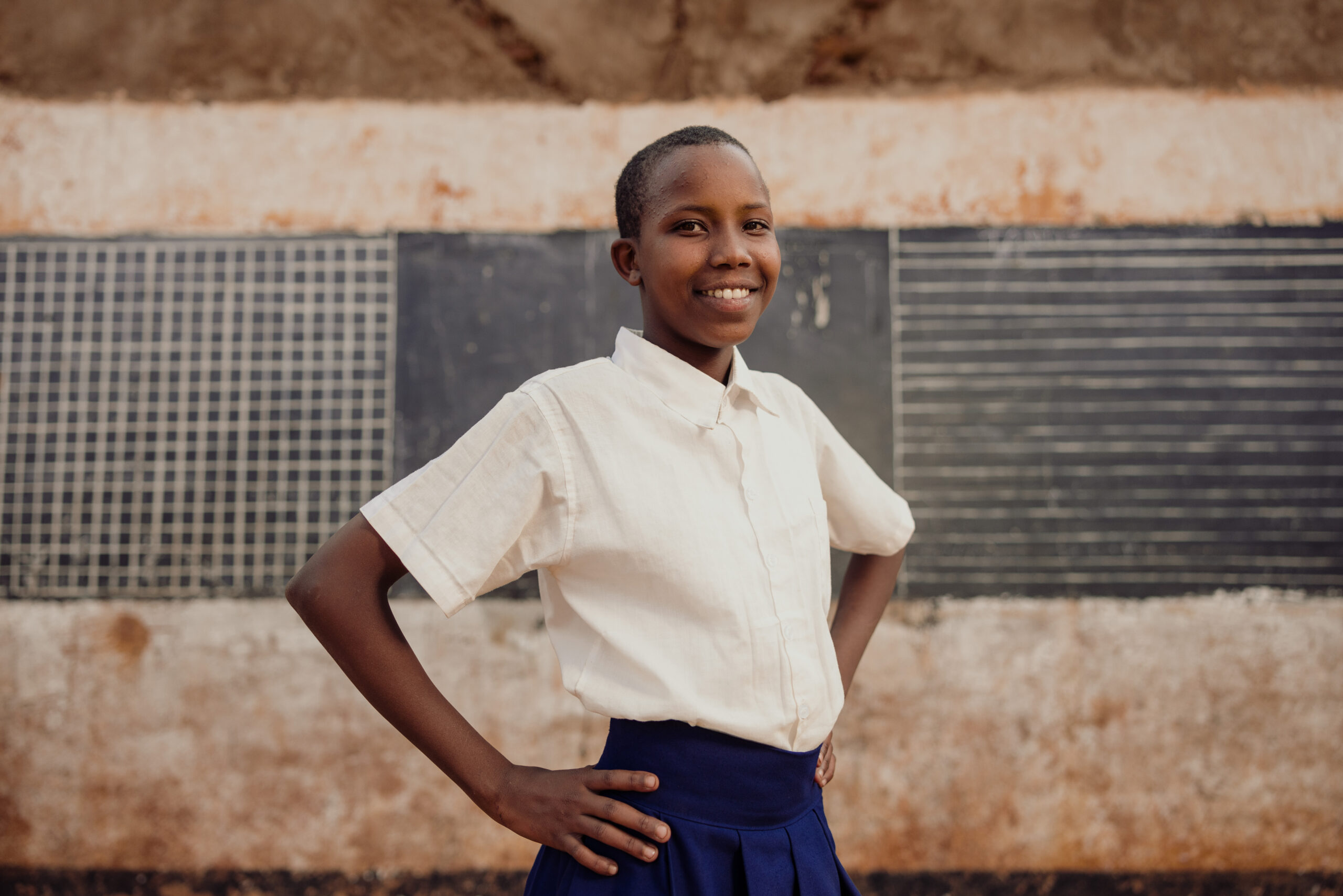 Glory from Tanzania stands with her hands on her hips in front of her school.