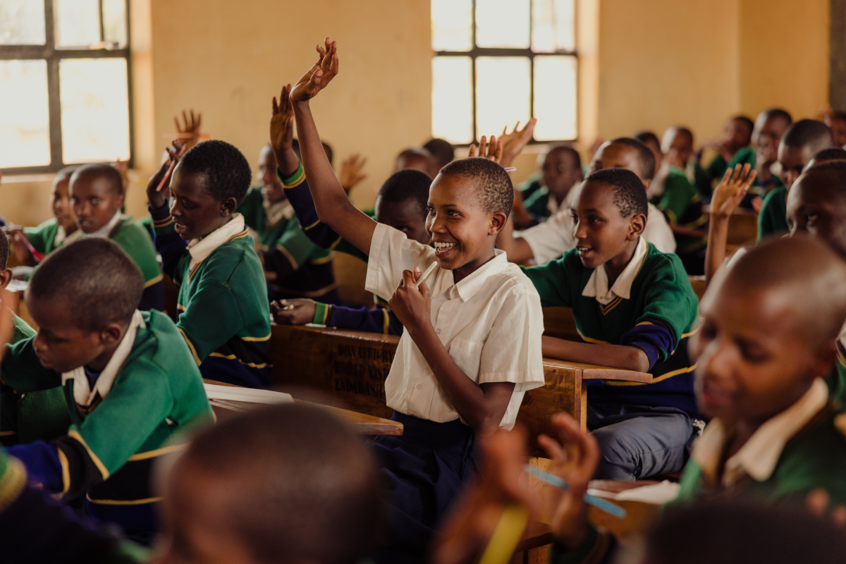 Happy to be attending school, Glory raises her hand to answer a teacher’s question in a classroom of students.
