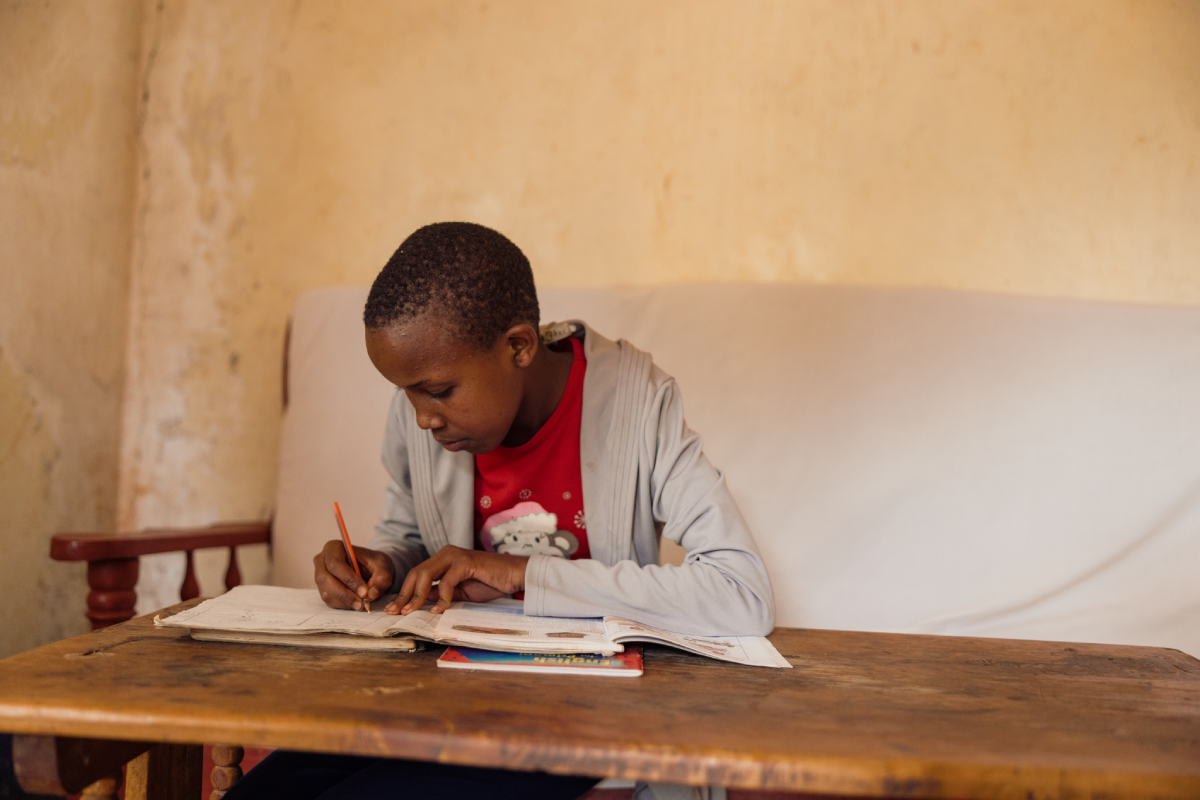 Glory sits at a table in her home, studying and completing homework.