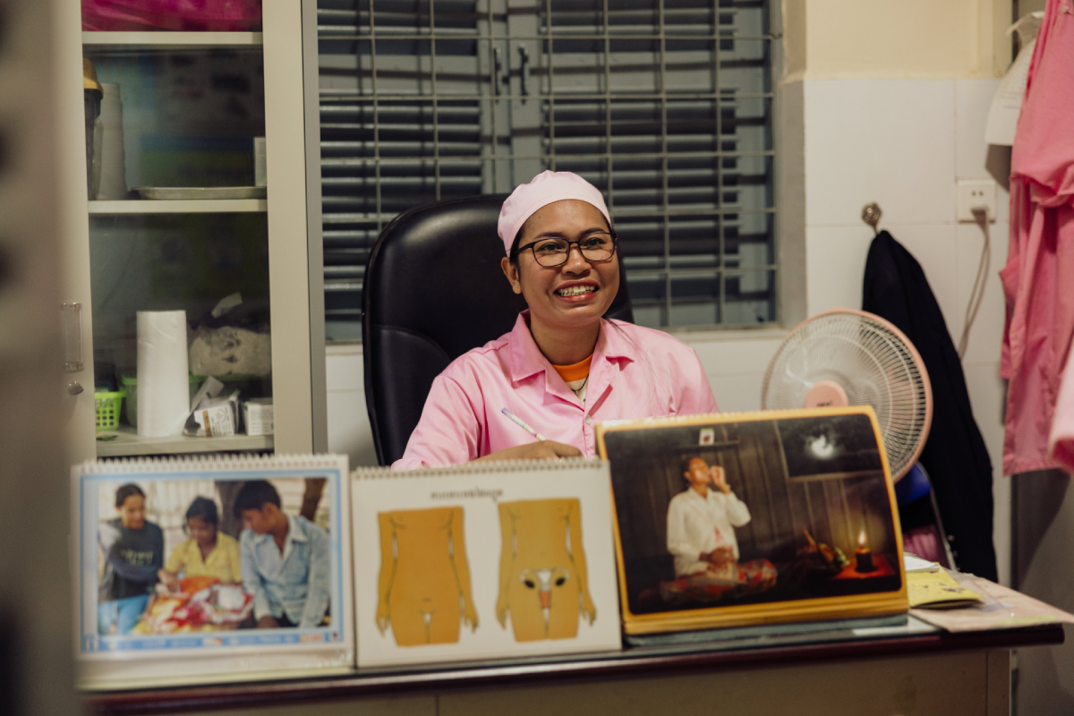 Brimming with a confident smile, Vannak sits at her desk with educational resources and diagrams for her work educating mothers on their health.