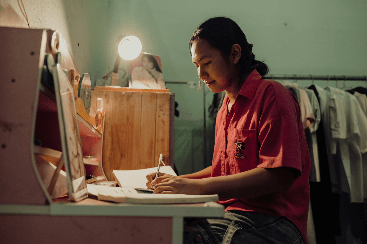 A teenage girl studying and writing at a desk in her bedroom.
