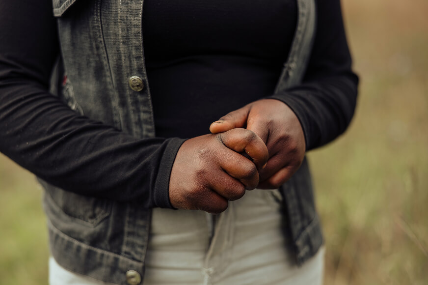 An adolescent girl in a jean jacket clasps her hands together in nervousness. 