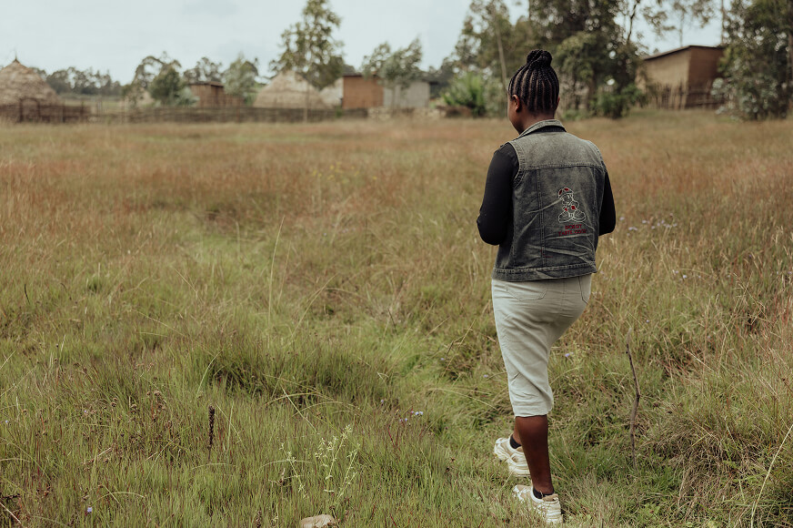 An adolescent girl who survived a rape attack, walks in a grassy field wearing a skirt and jean jacket near her village in Hulu, Ethiopia.